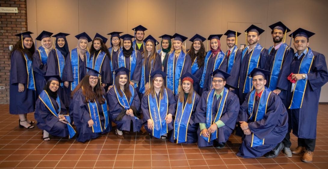 a large group of graduating students wearing blue gowns with blue and gold stoles and graduation caps.