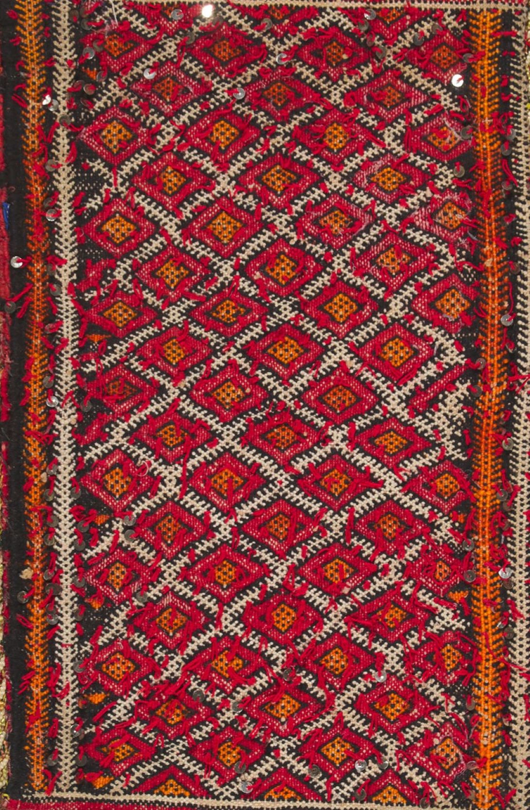 Moroccan tapestry in red, orange, brown, and white colors with two long bands on each side and diamond shapes in the middle.